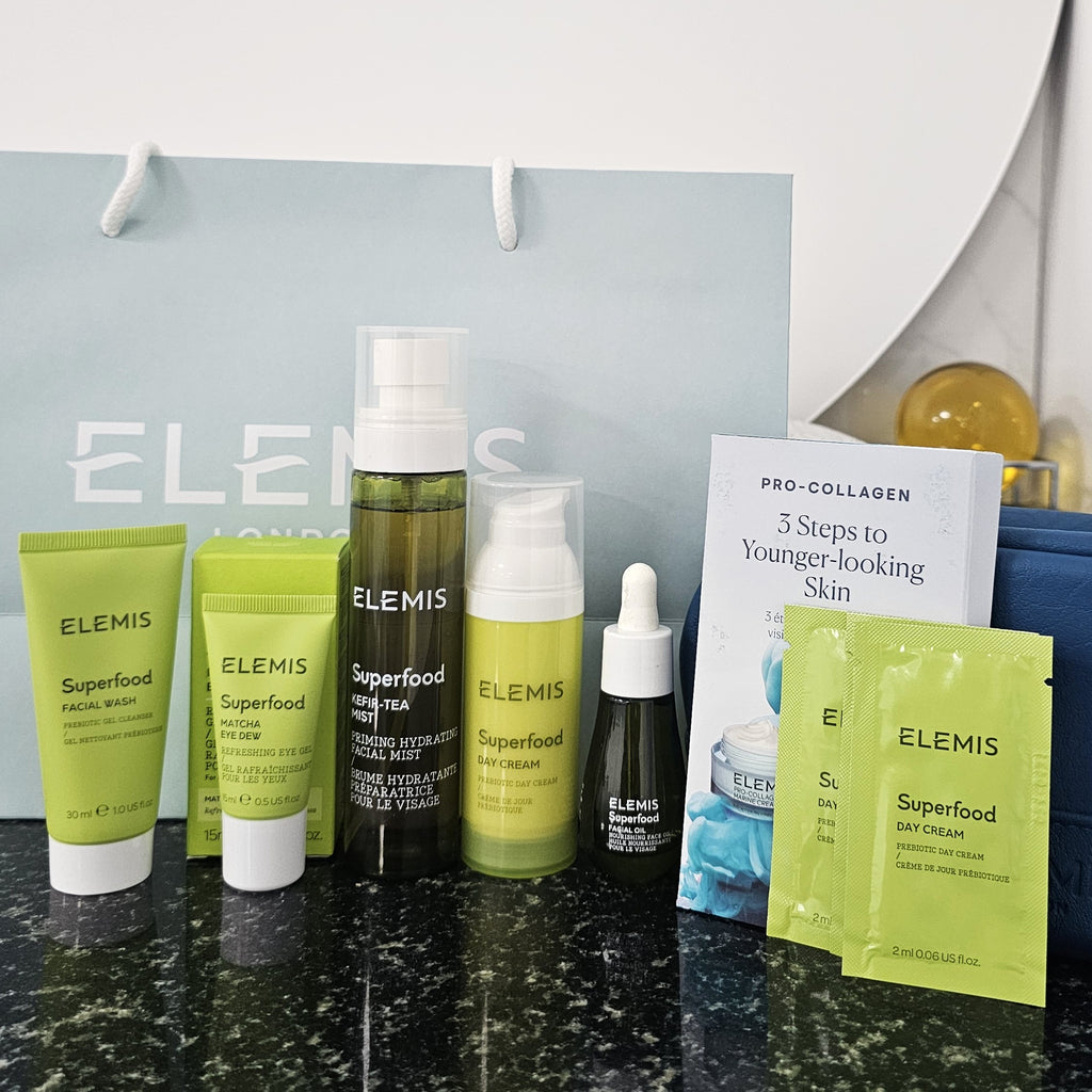 Elemis skincare products including bottles, tubes, and packets on a countertop with a branded bag in the background.